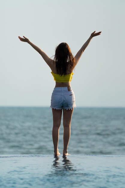 Asian Thai teenager female in Yellow relax and swim suit is posting on the infinity pool beside the sea beach in Thailand resort