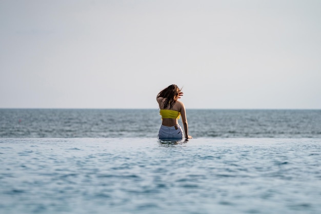 Asian Thai teenager female in Yellow relax and swim suit is posting on the infinity pool beside the sea beach in Thailand resort