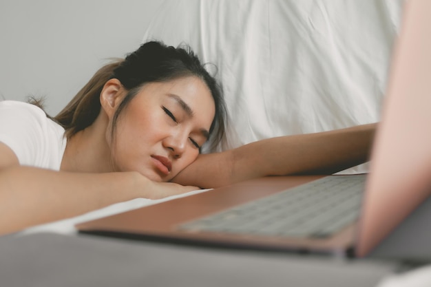 Asian thai woman fall asleep sleeping and resting head on her arm while working and using laptop on