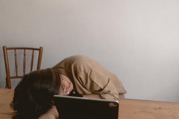 아시아 태국 여성이 낮잠을 자고 잠들고 작업하는 동안 머리를 팔에 고 노트북을 사용합니다.