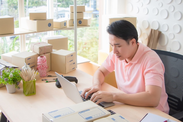 Asian Thailand Man typing documents on a computer laptop serious and often the repulsion on his desk filled with equipment used to pack the box and scan a barcode in the morning.