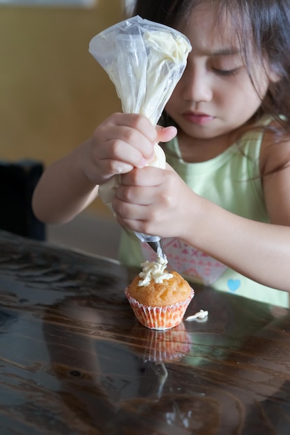 사진 아시아 유아 아이가 집에서 컵케이크를 장식하려고 합니다.