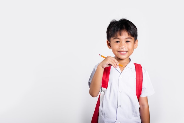 Pantaloni rossi dell'uniforme tailandese dello studente di usura felice sorridente del bambino asiatico che tengono la matita per il taccuino degli scrittori