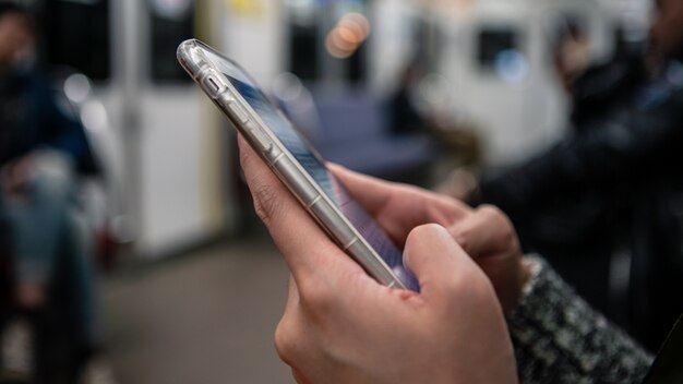 Asian tourist woman holds smartphone inside of metro. passenger\
using technology phone in subway. means of communication,\
fashionable gadget. lifestyle and transportation