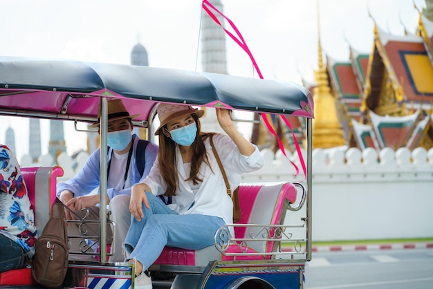 Asian tourists couple tuk tuk passenger native taxi driver to journey near Wat phra keaw in Bangkok, Thailand