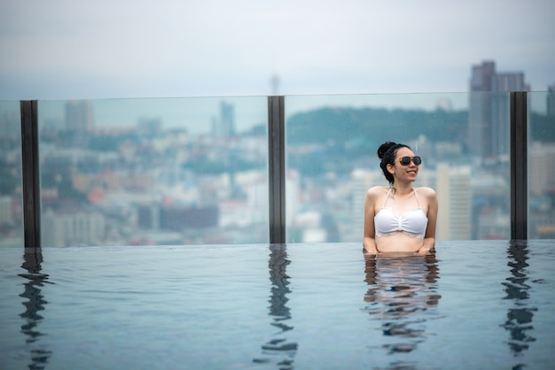 Foto concetto di viaggio asiatico. giovane donna che si gode con la vista del cielo della città dalla piscina sul tetto dell'hotel, lo stile di vita di una bella ragazza all'aperto durante le vacanze