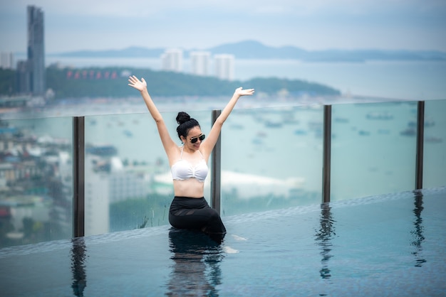 Photo asian travel concept. young woman enjoying with the city sky view from hotel roof top swimming pool, beautiful girl lifestyle outdoor in vacation time