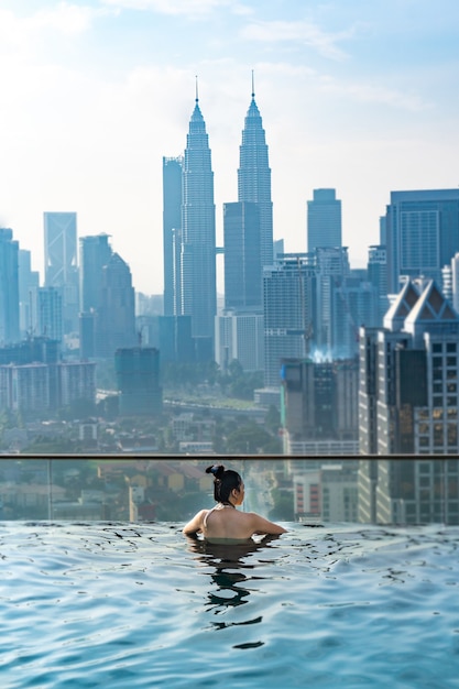 アジア旅行のコンセプト。ホテルの屋上プールから街の空の景色を楽しんでいる若い女性、休暇中に屋外の美しい女の子のライフスタイル