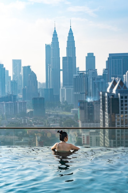 Asian travel concept. young woman enjoying with the city sky view from hotel roof top swimming pool, beautiful girl lifestyle outdoor in vacation time