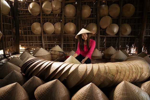 Artigiano femminile del viaggiatore asiatico che fa il cappello tradizionale del vietnam nella vecchia casa tradizionale