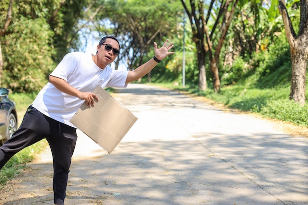 Asian traveler man catches the car on the road while holding a blank board