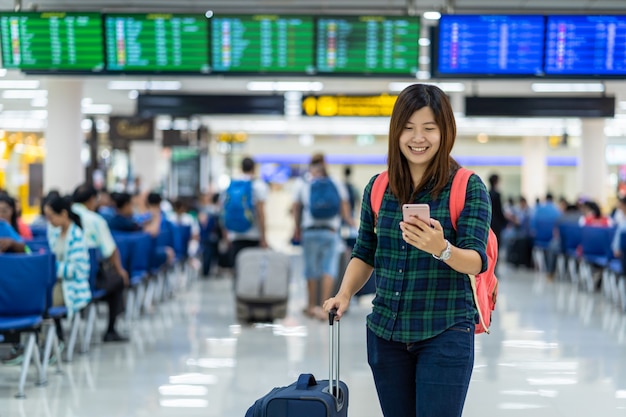 Азиатский путешественник с багажом держит умный мобильный телефон для регистрации на рейс