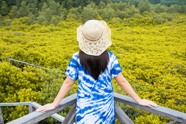 Foto donna viaggiatrice asiatica che tiene il cappello e si trova su un ponte di legno per viaggiare