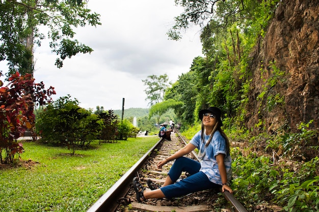 Азиатские путешественники, тайские женщины, путешествуют в гости и позируют портрет на поезде, чтобы сфотографироваться и осмотреть пейзаж реки Квай в национальном парке водопада Сай Йок в пещере Тхам Красае в Канчанабури, Таиланд