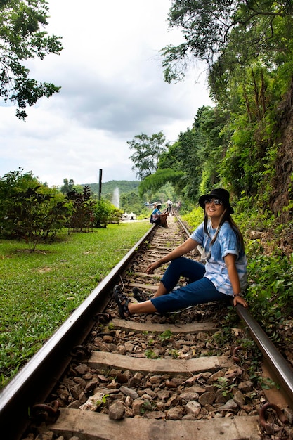 태국 칸차나부리의 탐 크라사에 동굴에 있는 사이욕 폭포 국립공원의 콰이강 풍경을 감상하고 사진을 찍기 위해 트랙 기차를 방문하고 사진을 찍는 아시아 여행자 태국 여성