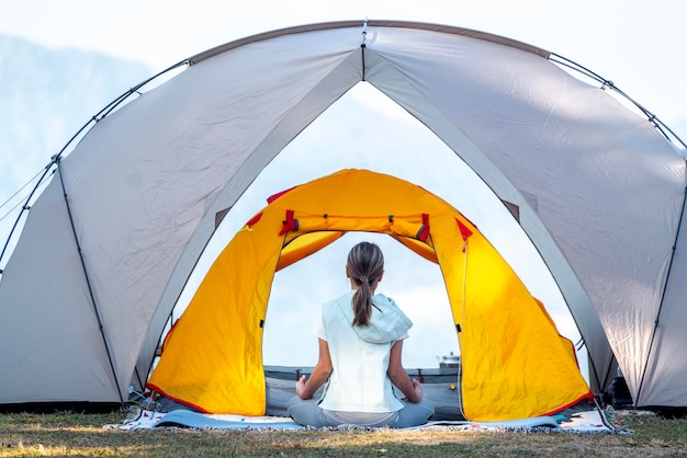 Asian traveller woman post yoga in tent on her camping with mountain and outdoor background