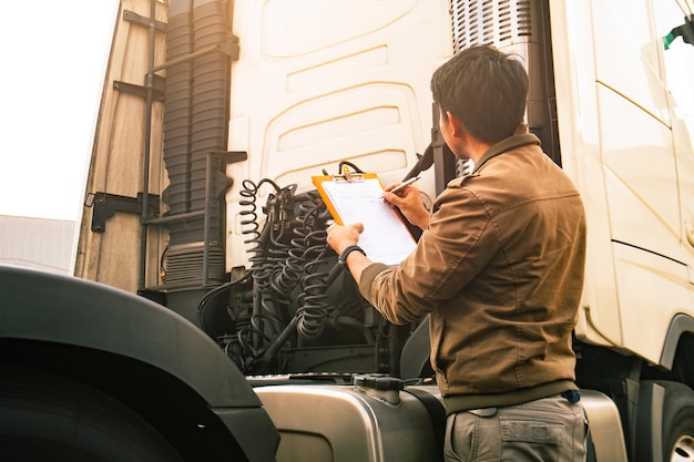 Asian truck driver holding clipboard inspecting safety vehicle maintenance checklist of modern semi truck.