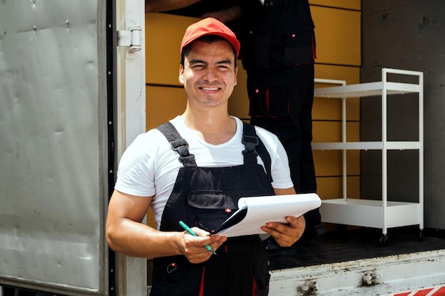 Photo asian truck driver wearing red cap holding a clipboard checking the delivery packages checklists