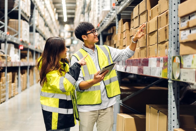 I dettagli dell'ordine di spedizione del team di due ingegneri asiatici su tablet controllano le merci e le forniture sugli scaffali con l'inventario di base delle merci nell'industria logistica di fabbrica e nell'esportazione aziendale