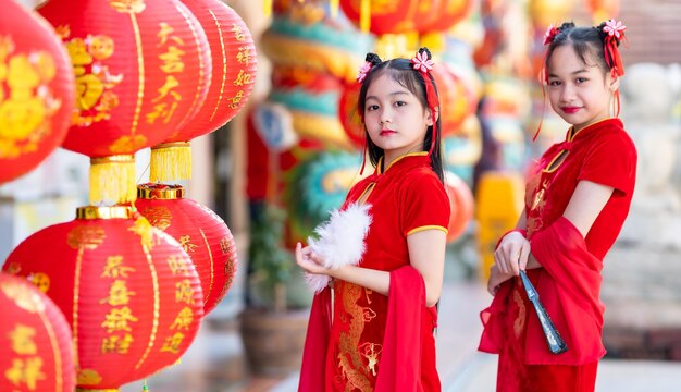 Due ragazze asiatiche che indossano una decorazione cheongsam cinese tradizionale rossa con in mano un ventaglio cinese e lanterne con il testo cinese benedizioni scritte su di esso è una benedizione della fortuna per il capodanno cinese