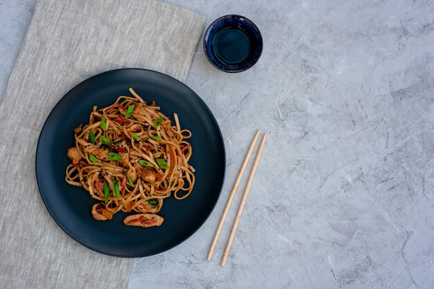 Asian udon noodles with chicken vegetables and teriyaki sauce on a black wooden background