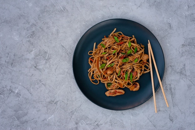 Asian udon noodles with chicken vegetables and teriyaki sauce on a black wooden background