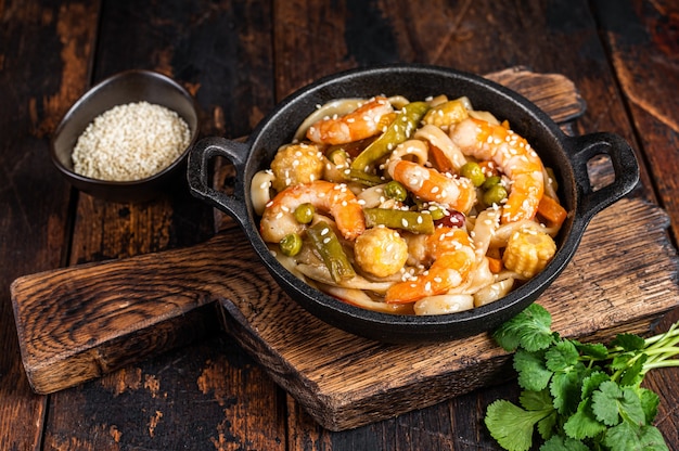 Asian Udon stir-fry noodles with shrimps prawns in a pan. Dark wooden background. Top view.