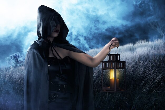 Asian witch woman with a black cloak holding a lantern standing on the field