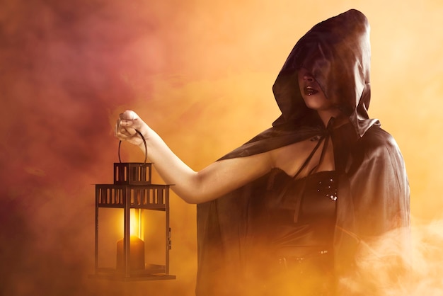 Asian witch woman with a black cloak holding a lantern standing with dramatic background