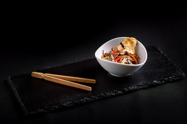 Asian with miso pasta, soy sauce, herbs. On a black stone table, with chopsticks.