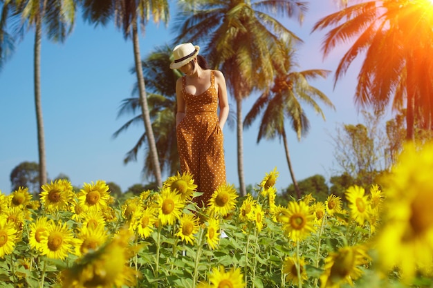 Азиатская женщина 40-х годов ЛГБТ-трансгендер выражает чувство счастливой улыбки весело под солнцем в желтом цветочном поле подсолнечника над горой голубого неба Женщина позирует для модной съемки на открытом воздухе