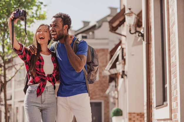 Asian woman and african american man taking selfie on the camera on the street