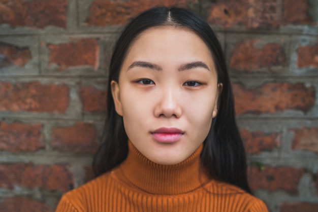 Asian woman against brick wall.