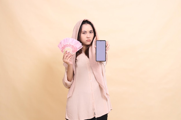 Photo asian woman angry carrying rupiah money and holding her cellphone gadget screen in front of her beau