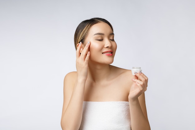 Asian woman applying cosmetic cream on skin on isolated white background