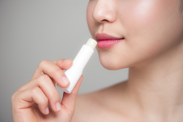 Photo asian woman applying hygienic lip balm over grey background