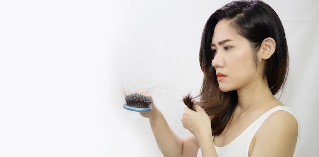 Азиатская женщина смотрит на выпадение волос и с беспокойством держит синюю расческу и волосы