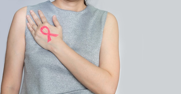 Asian woman are show Pink ribbon which draw by lip stick on back hand and touch breast to encourage breast cancer patient Breast cancer campaign in October month