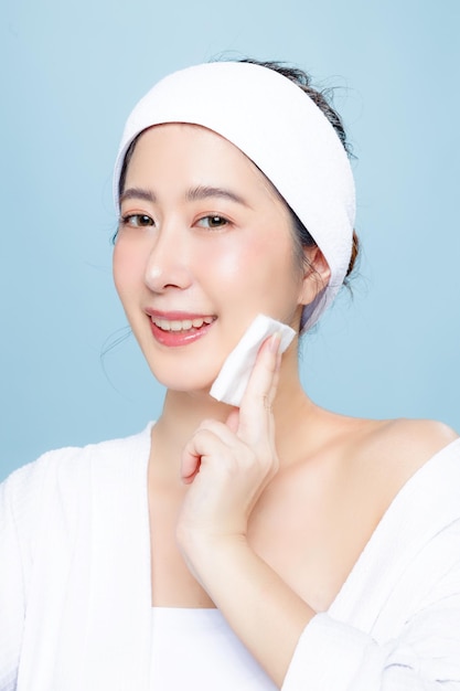 Asian woman in bathrobe with perfect clear skin Happy girl model with fresh hydrated facial and natural makeup on isolated blue background Cosmetology beauty and spa wellness Plastic surgery