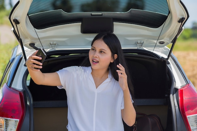 Азиатская женщина рядом с автомобилем с помощью смартфона