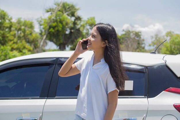 Donna asiatica accanto a un'auto utilizzando lo smartphone