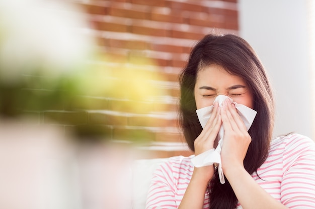 asian woman blowing her nose on couch
