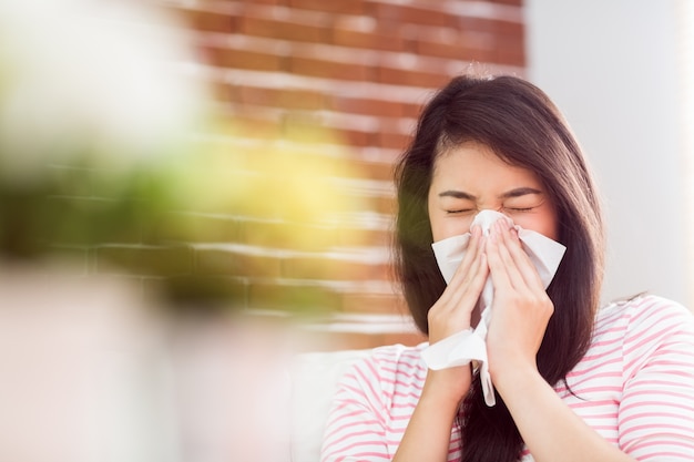 Asian woman blowing her nose on couch