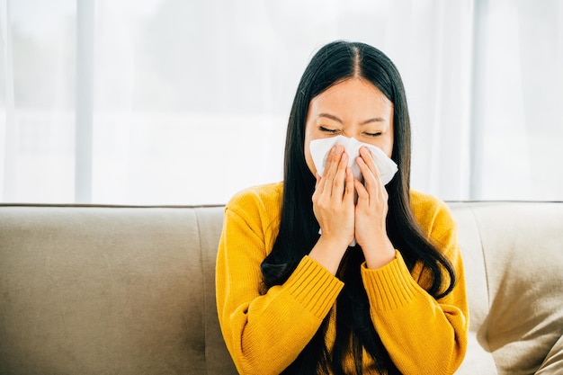 Photo asian woman blowing her nose holding a handkerchief experiencing flu symptoms at home