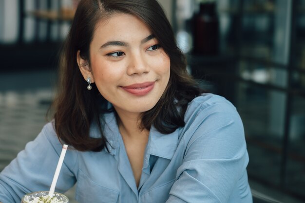 Donna asiatica in camicia blu nel caffè bevente del caffè e parlare con il sorriso dell'amico e il fronte felice