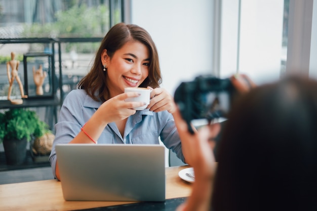 コーヒーを飲みながら、ボーイフレンドの笑顔と幸せそうな顔と話しているカフェで青いシャツのアジア女性