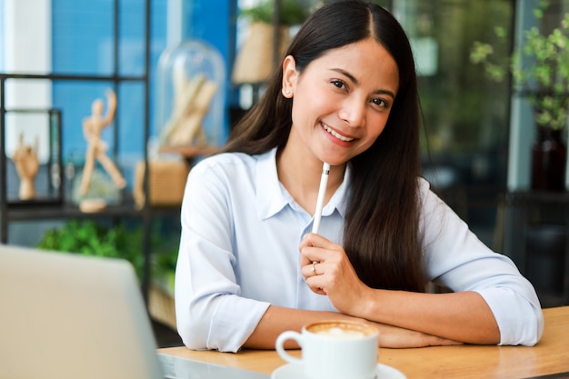 Asian woman in blue shirt working and drink coffee in coffee shop cafe