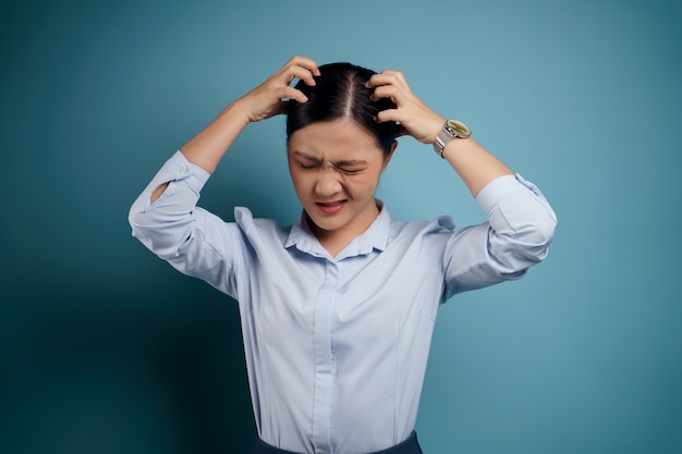 Asian woman bored and annoyed, scratching her head, isolated on blue.