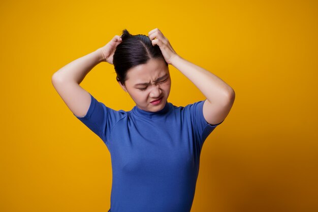 Asian woman bored and annoyed, scratching her head, on yellow.