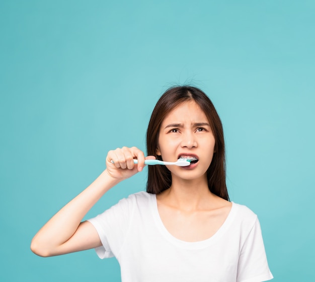 Donna asiatica che pulisce i denti su uno sfondo blu, concetto di igiene orale e assistenza sanitaria.